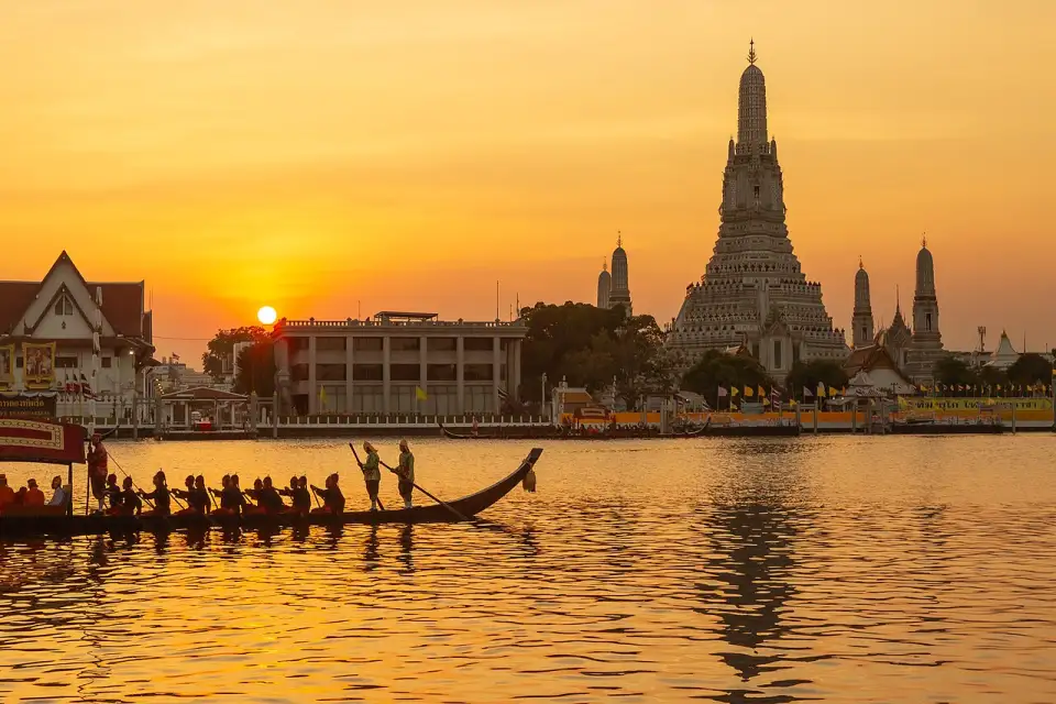 Wat Arun al atardecer con una barca real de remeros en primer plano sobre el río Chao Phraya