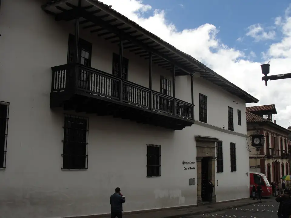 Fachada blanca de la Casa de Moneda con su balcón corrido de madera en la calle 11