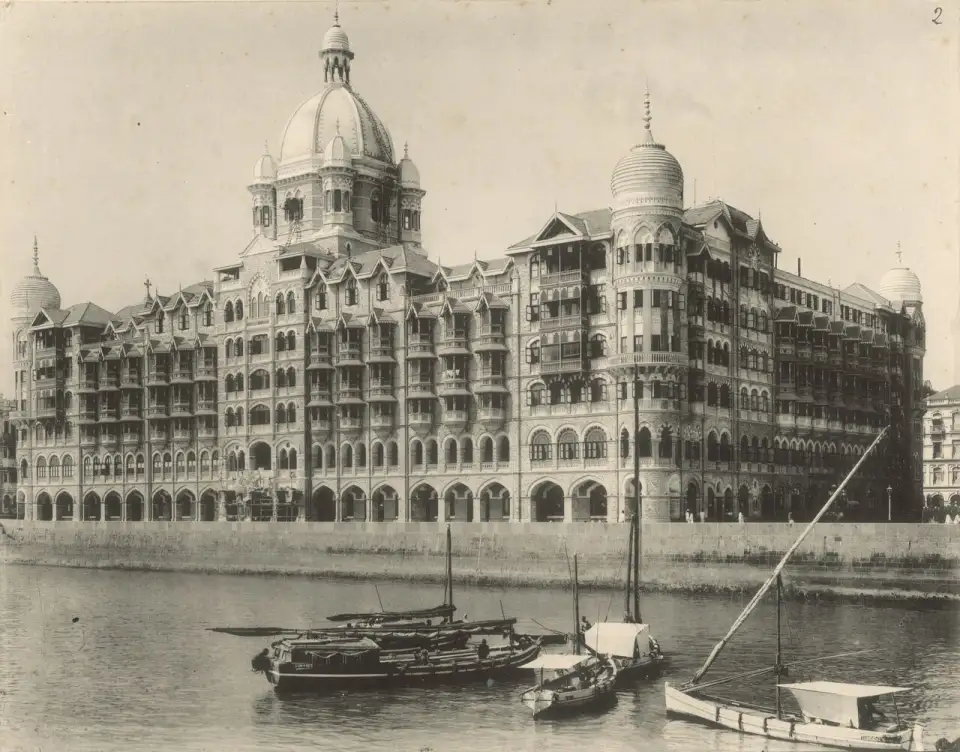 Fotografia antiga em preto e branco do hotel Taj Mahal visto do mar, com barcos à frente