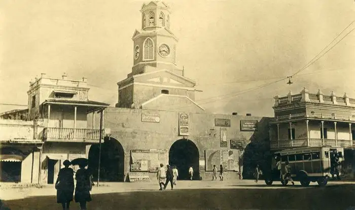 Old photograph of the Clock Tower Gate with passers-by and balconied buildings