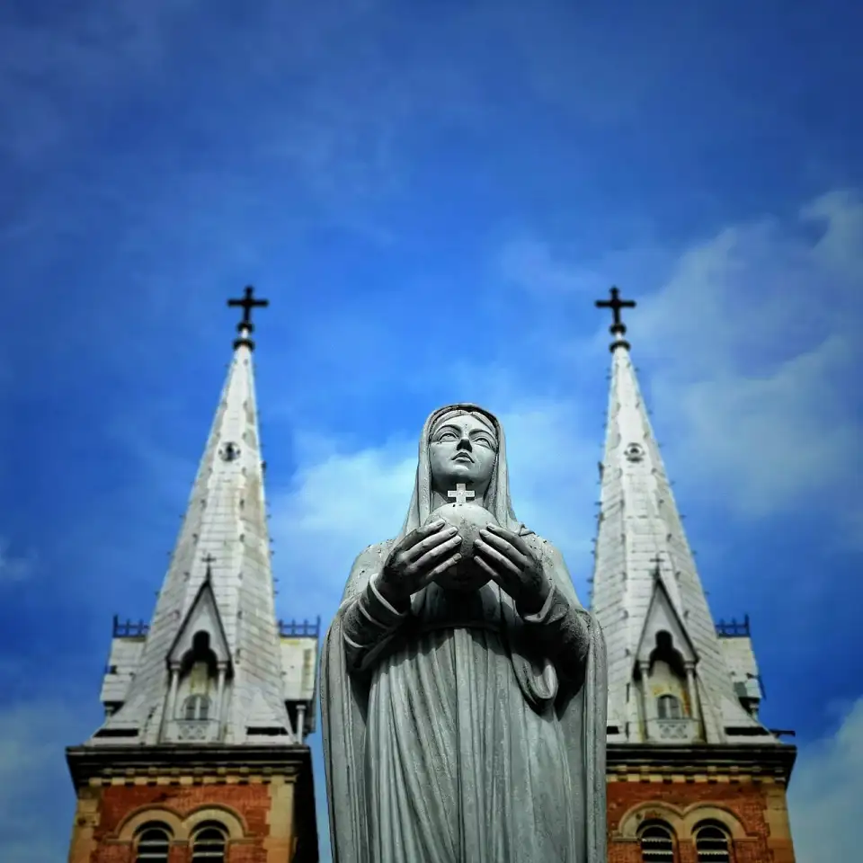 Close da estátua de mármore da Virgem, com as agulhas da catedral ao fundo