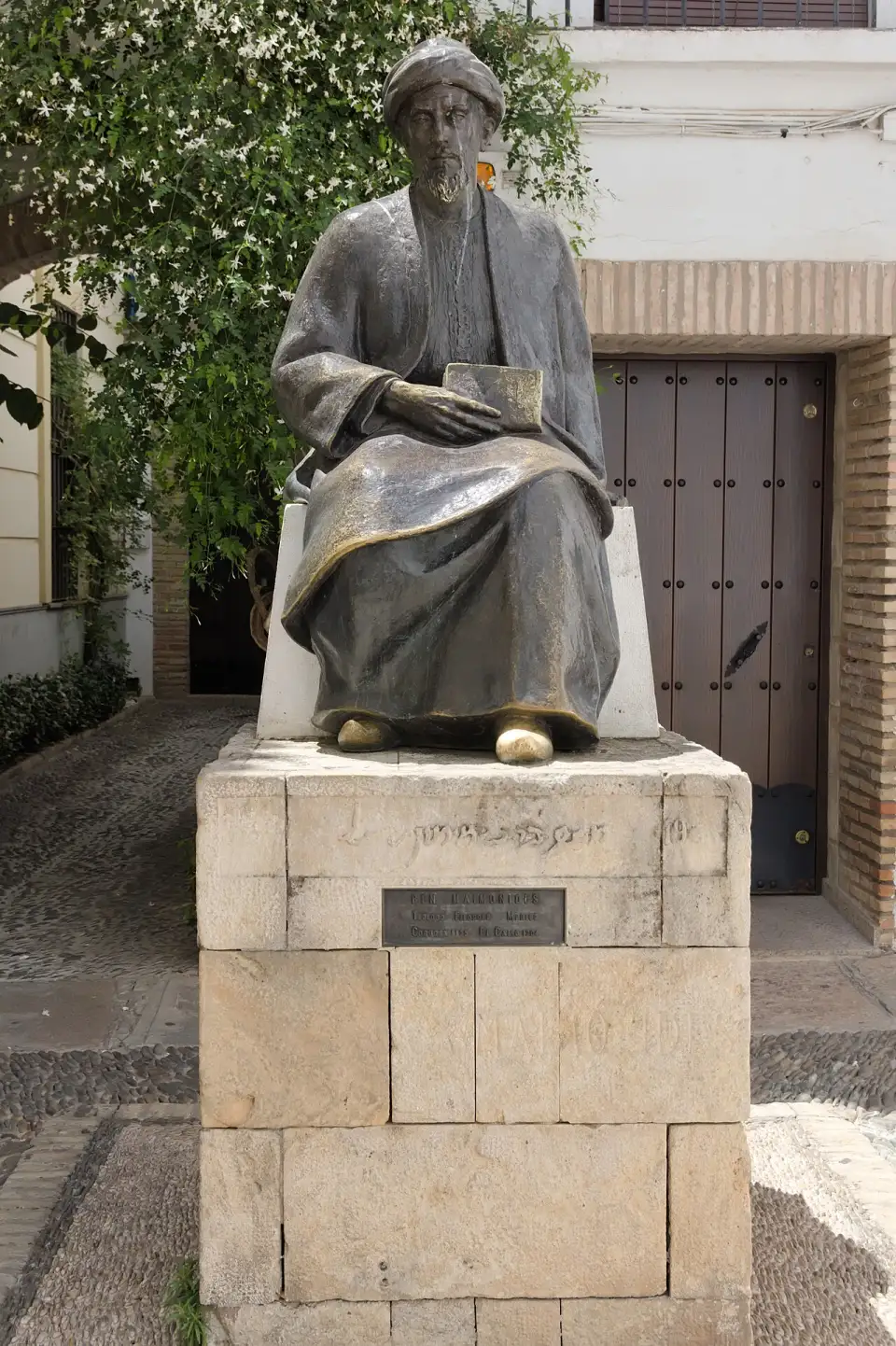 Seated bronze statue of Maimonides wearing a turban and holding a book, on a stone pedestal in Plaza de Tiberíades