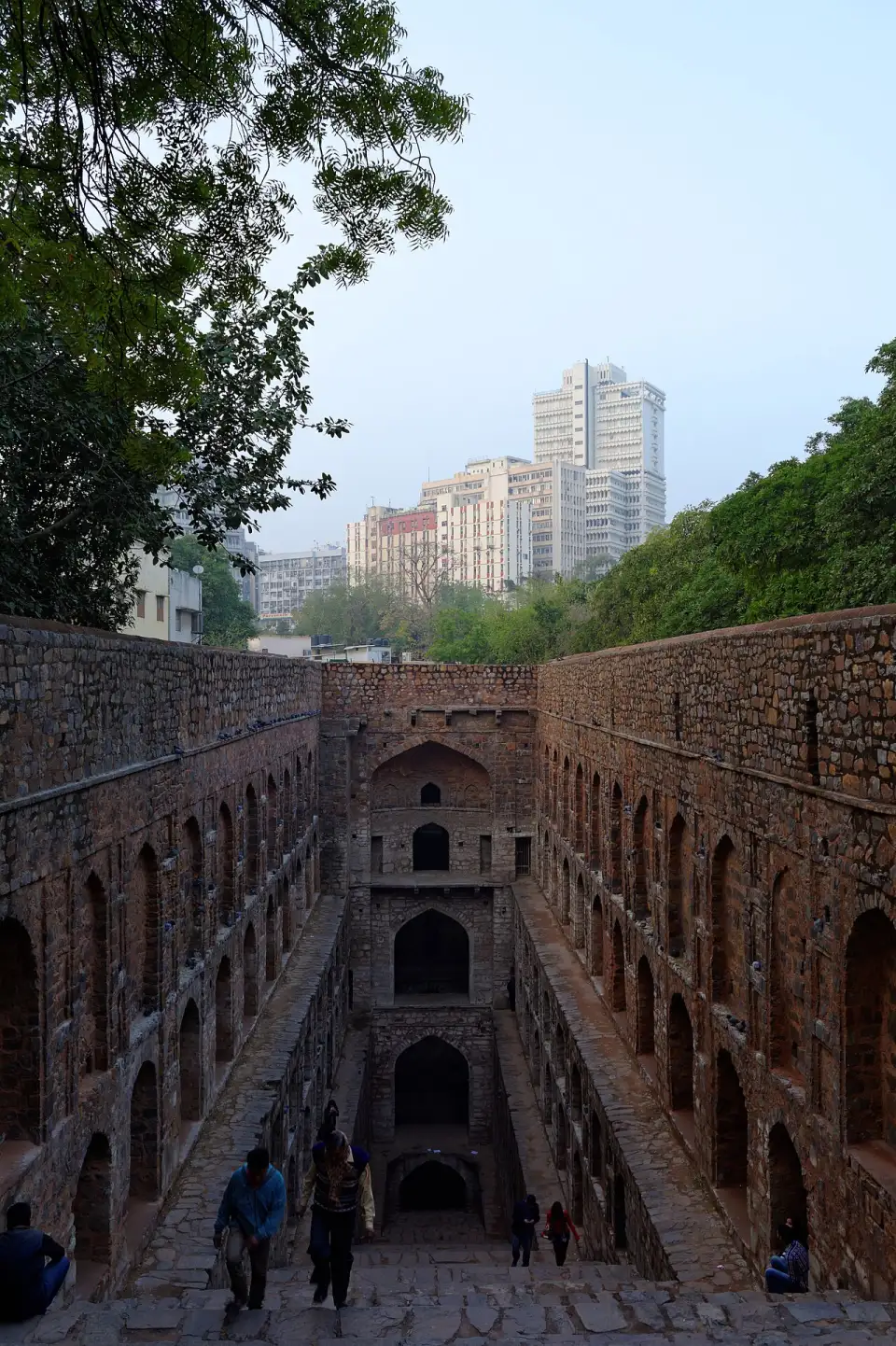 Steps of Agrasen ki Baoli between arched walls, with modern buildings behind