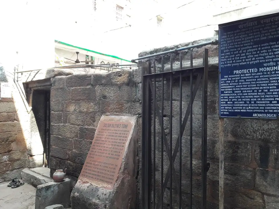 Entrada de la tumba de Razia Sultan con verja, lápida y cartel azul de la ASI