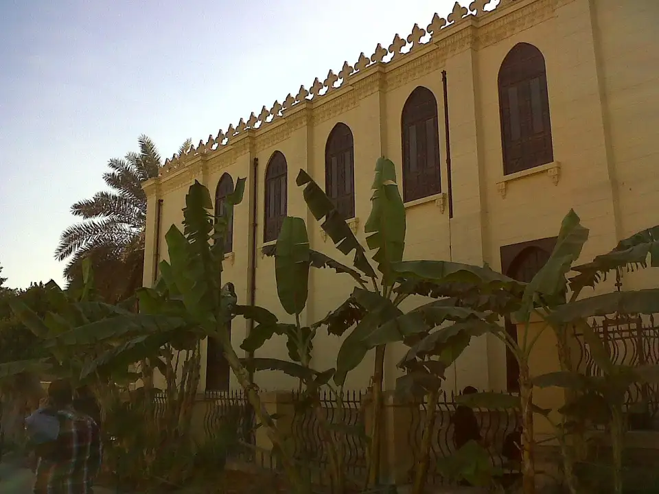 Fachada ocre da sinagoga Ben Ezra com janelas em arco e ameias, entre bananeiras