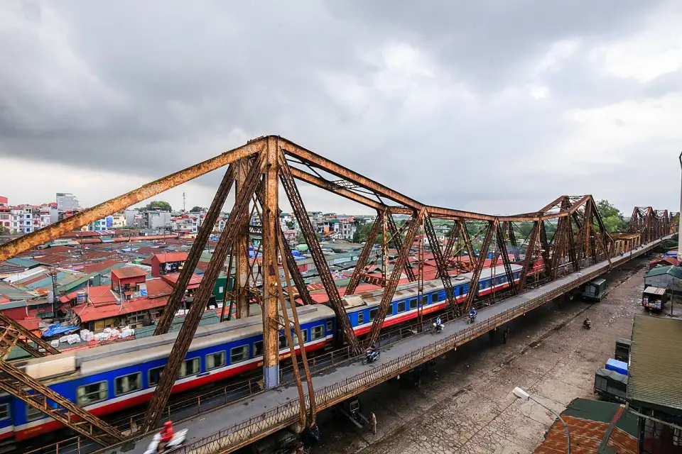 Iron girders of Long Biên Bridge with a train crossing above the rooftops