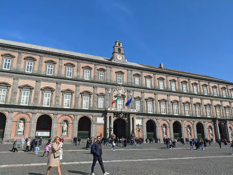 Fachada vermelha e cinza do Palácio Real de Nápoles com as estátuas dos reis nos nichos