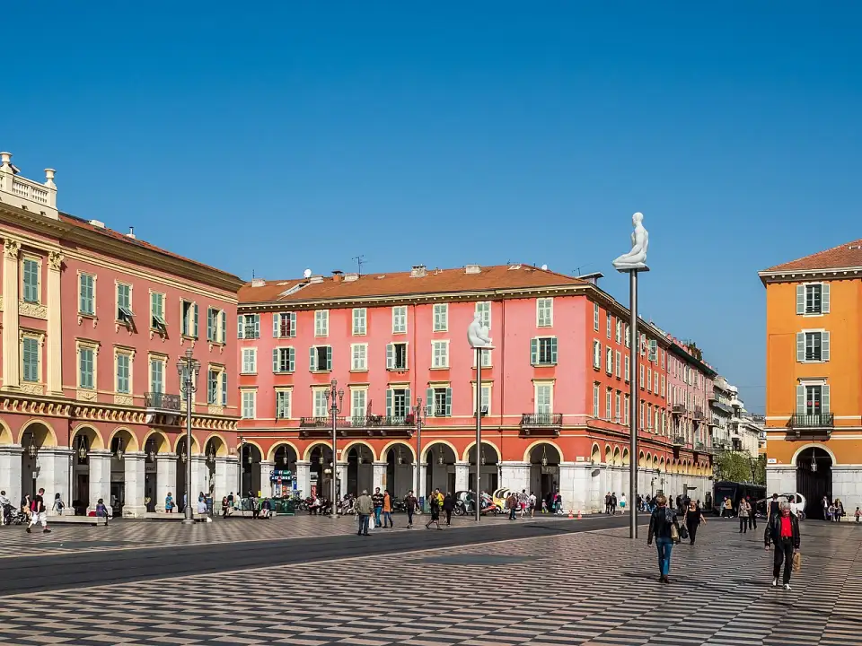 Praça Masséna com seus prédios vermelhos com arcadas, o piso quadriculado e uma figura de Plensa sobre um poste