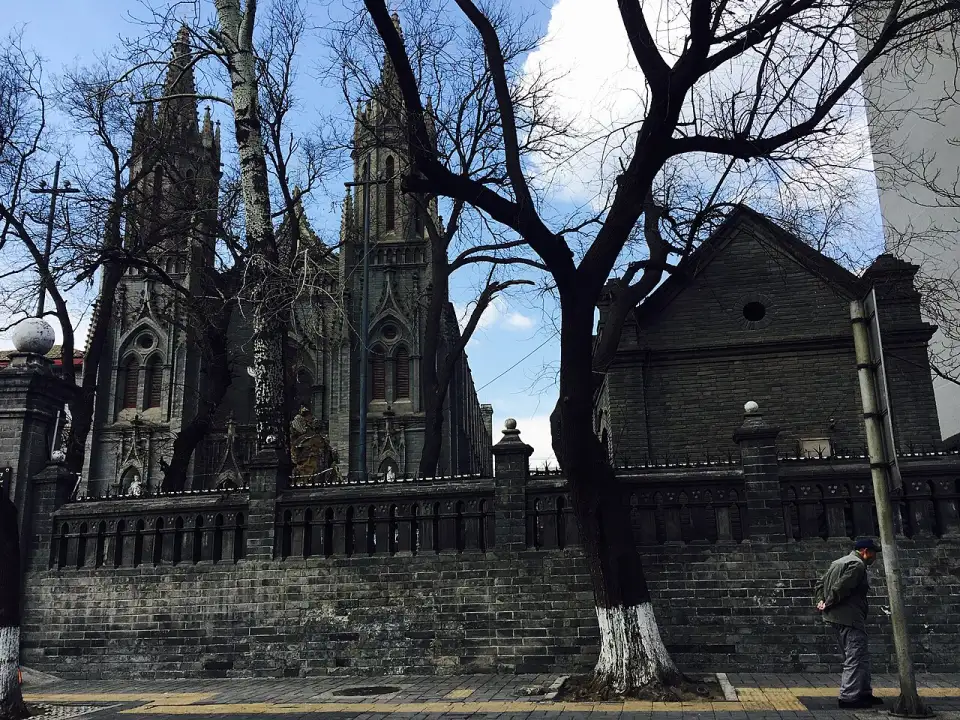 Die neugotische Michaelskirche mit ihren zwei grauen Turmspitzen hinter einer Ziegelmauer in der Dongjiaominxiang