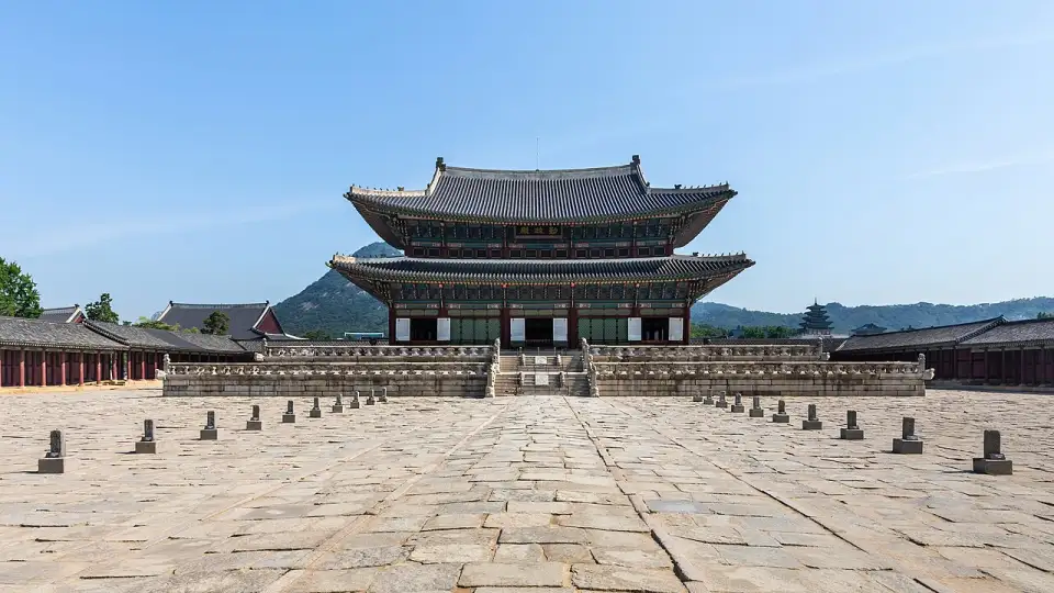 El salón del trono Geunjeongjeon del palacio Gyeongbokgung, de dos pisos y tejados curvos, ante un gran patio de piedra y la montaña al fondo
