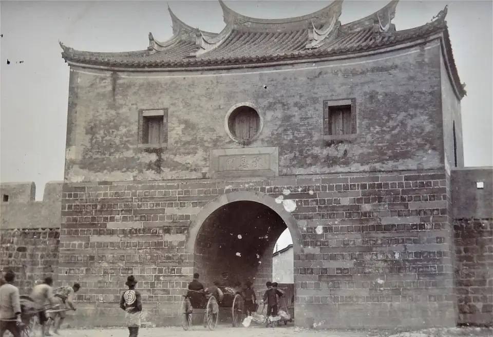 Old photograph of the North Gate with its arch, the city wall on either side and a cart passing in front