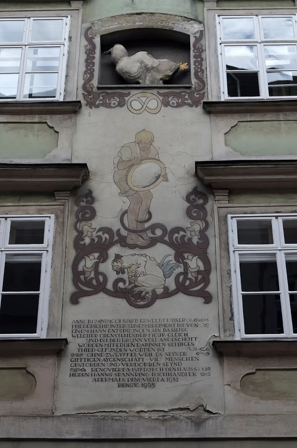 La figure de pierre du basilic dans sa niche, au-dessus de la peinture du jeune homme au miroir et de l'inscription